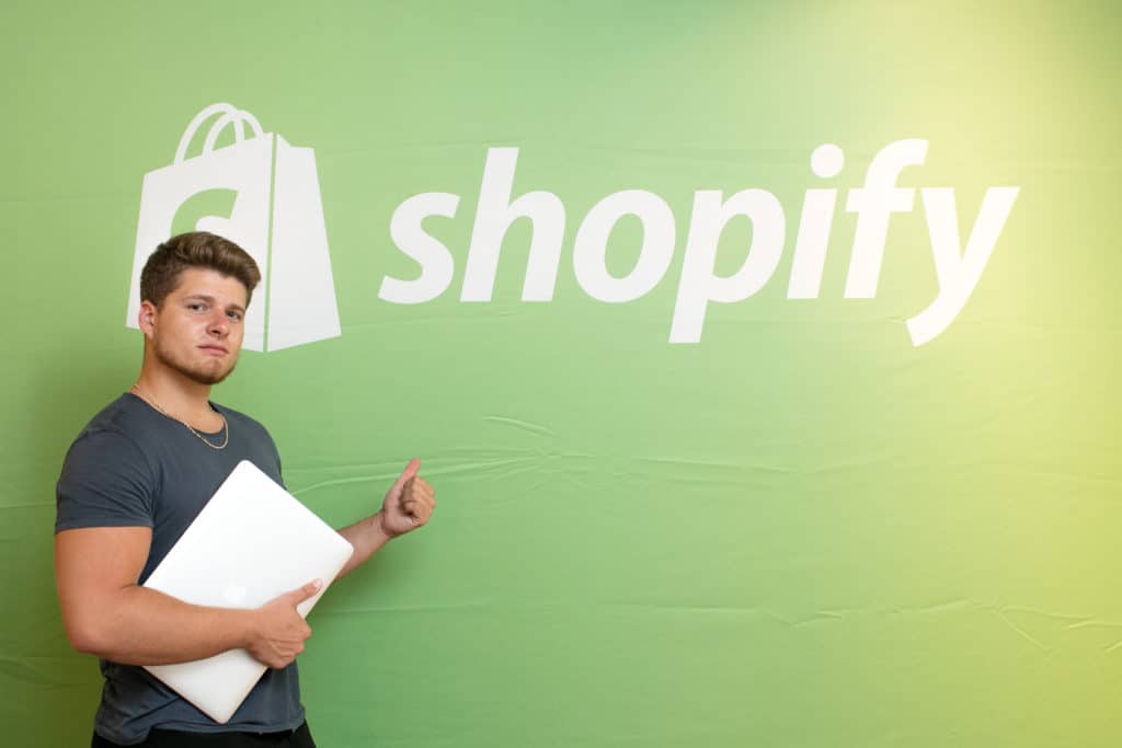 Visual of Justin Woll in front of a Shopify sign
